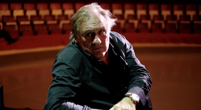 Gerard Depardieu im Saal Gerard Depardieu im Scheinwerferlicht, er trägt ein schwarzes Hemd, er lächelt